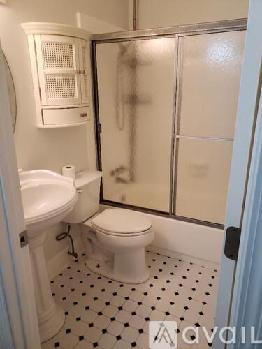 A white toilet sits in a bathroom with a sink and a shower.