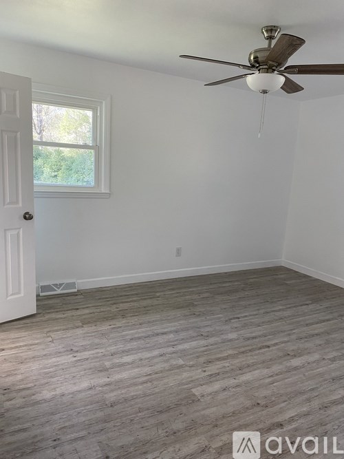 A room with a ceiling fan and a window with a view of trees.