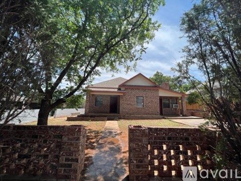 A house with a brick wall and trees in front.