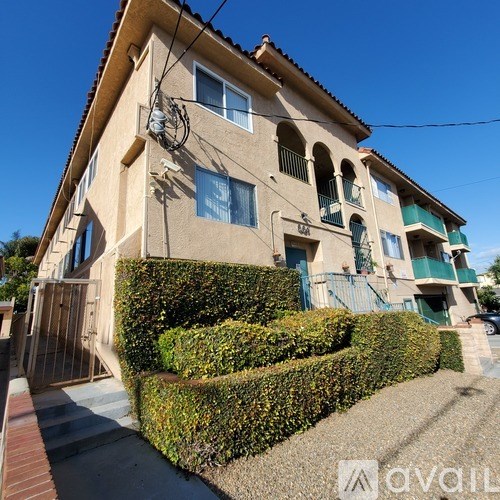 A beige house with green shutters and a hedge in front.