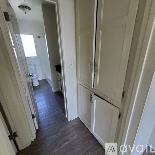 A hallway with a white door and a toilet in the background.