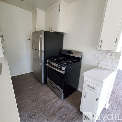A kitchen with a black fridge and stove, white cabinets, and a white countertop.