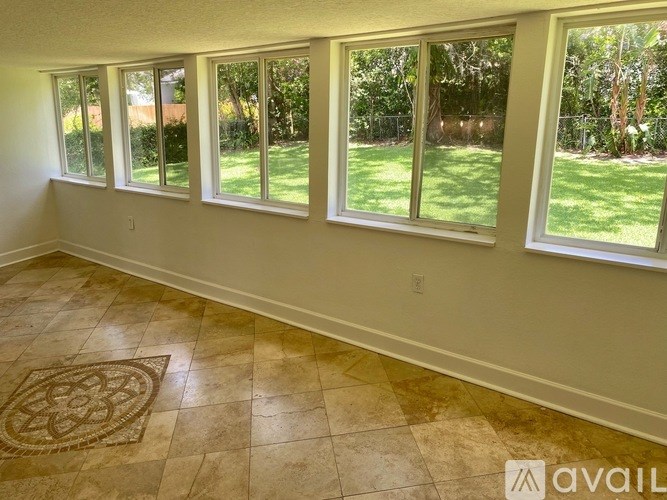 A room with a tiled floor and a rug in front of a row of windows.