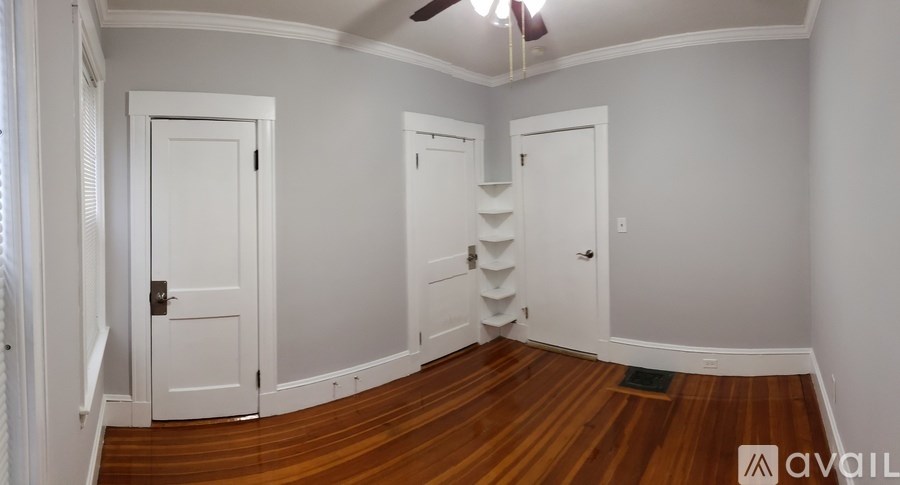 A room with white walls and wooden floors has two doors and a staircase.