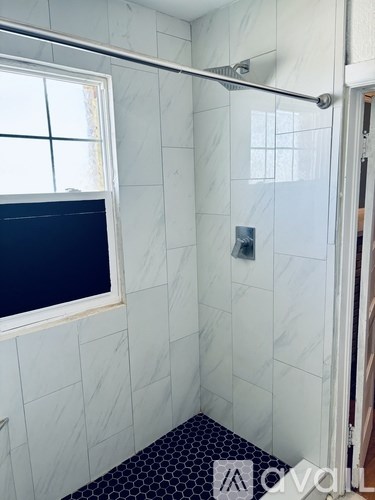 A white tiled bathroom with a window and a shower.