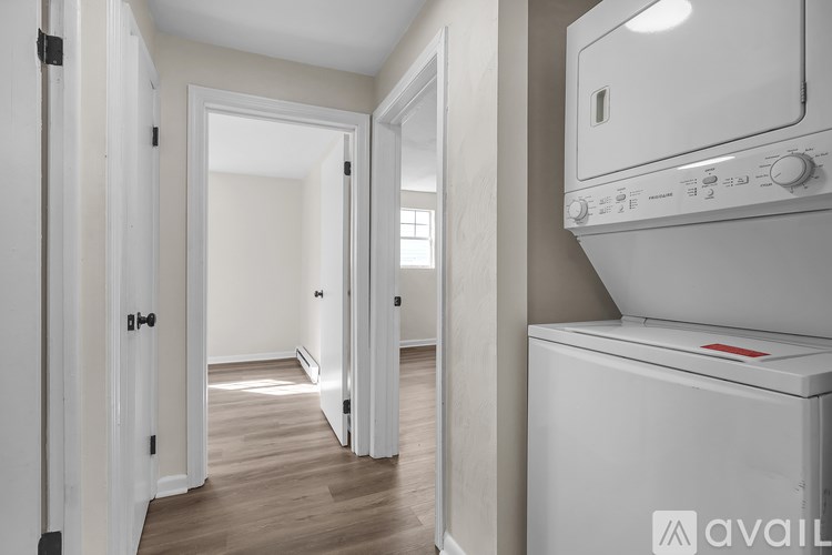 A white washing machine is in a room with white walls and wooden floors.