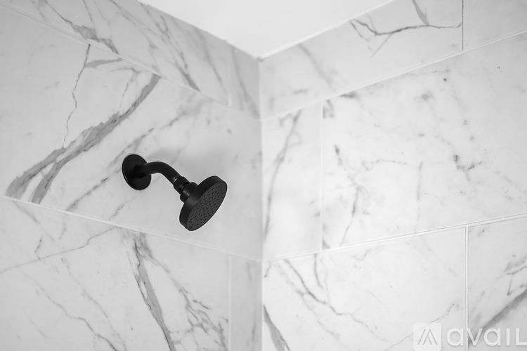 A black shower head mounted on a white marble wall.