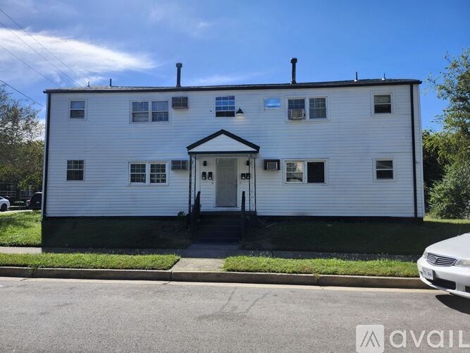 A white two-story house with a black roof and a car parked in front.