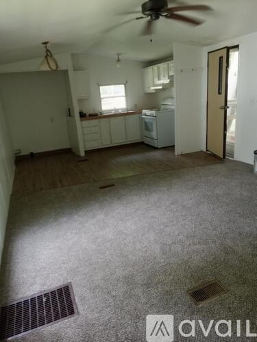 A room with a ceiling fan and a kitchen area in the background.