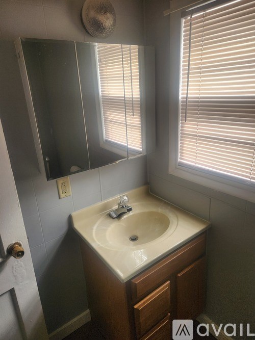 A bathroom with a sink, mirror, and a window with blinds.