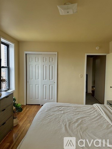 A bedroom with a white bed, dresser, and door.