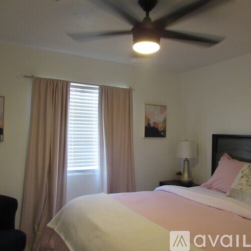 A bedroom with a bed, a ceiling fan, and a window with curtains.