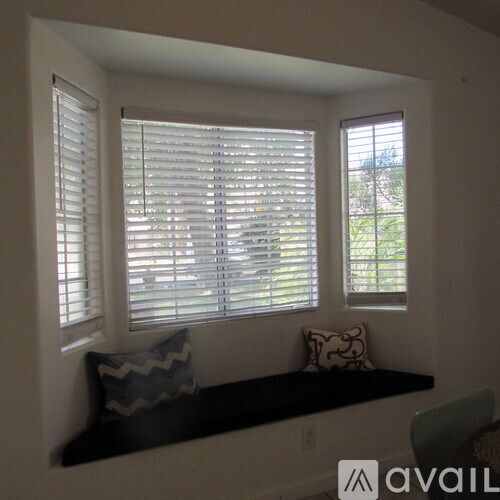 A window with white blinds and a black bench with a pillow on it.