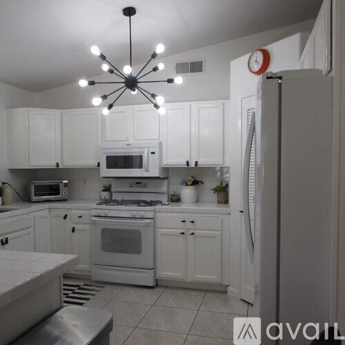A kitchen with white cabinets and appliances, a stainless steel refrigerator, and a ceiling fan with lights.