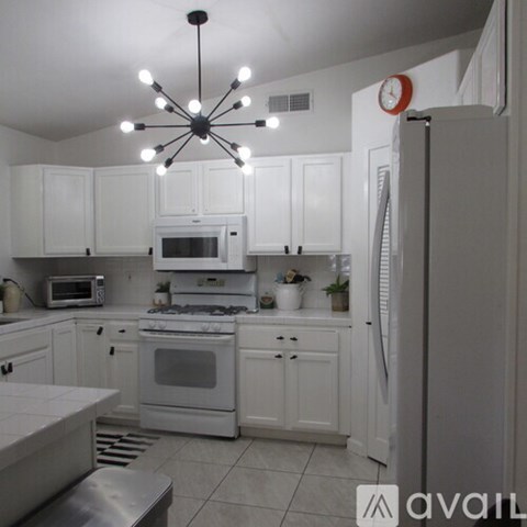 A kitchen with white cabinets and appliances, a stainless steel refrigerator, and a ceiling fan with lights.