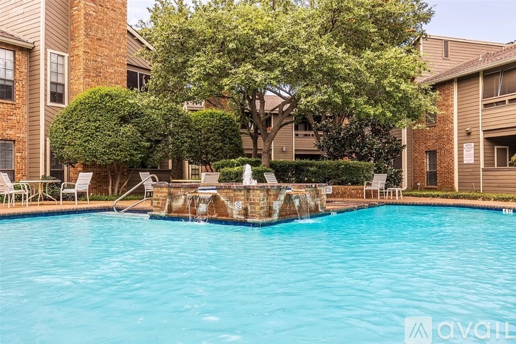 A pool with a waterfall surrounded by chairs and trees.