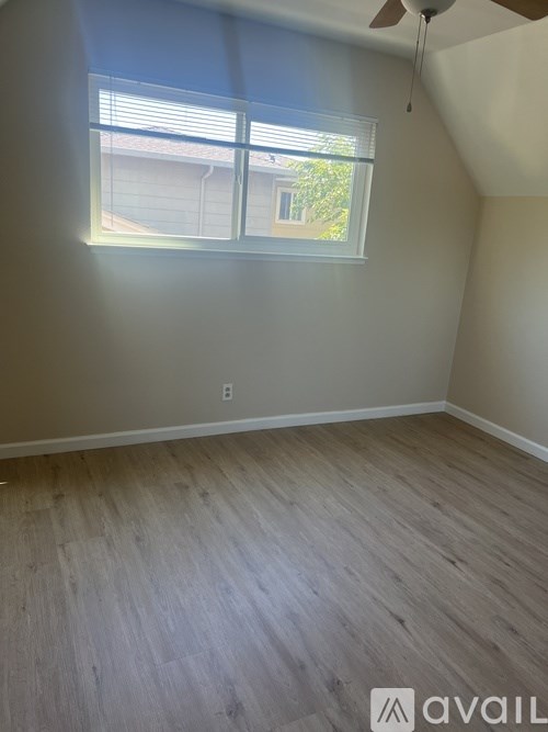 A room with a ceiling fan and a window letting in sunlight.
