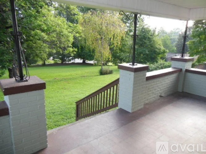 A balcony with a brick pillar and a metal railing overlooks a green lawn.