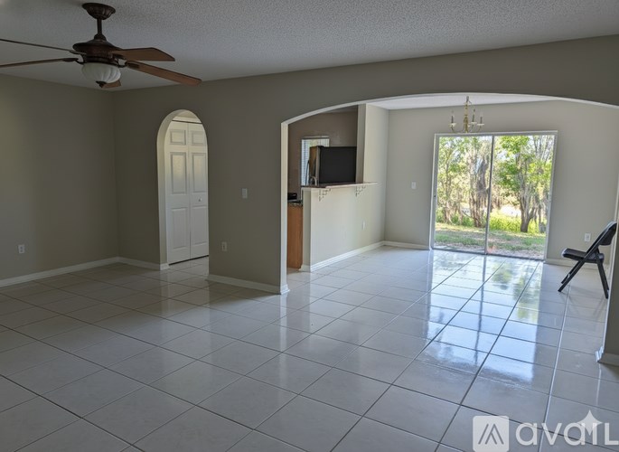 A spacious room with a ceiling fan and a sliding glass door leading to a backyard.
