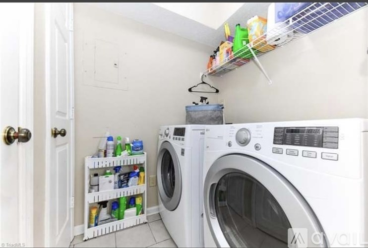 A white washing machine sits in a laundry room with a shelf above it.