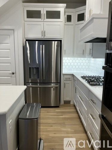 A kitchen with a stainless steel refrigerator and a trash can.