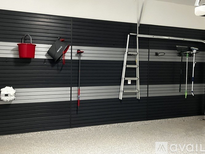 A red bucket hangs on a black wall next to a ladder and a black speaker.