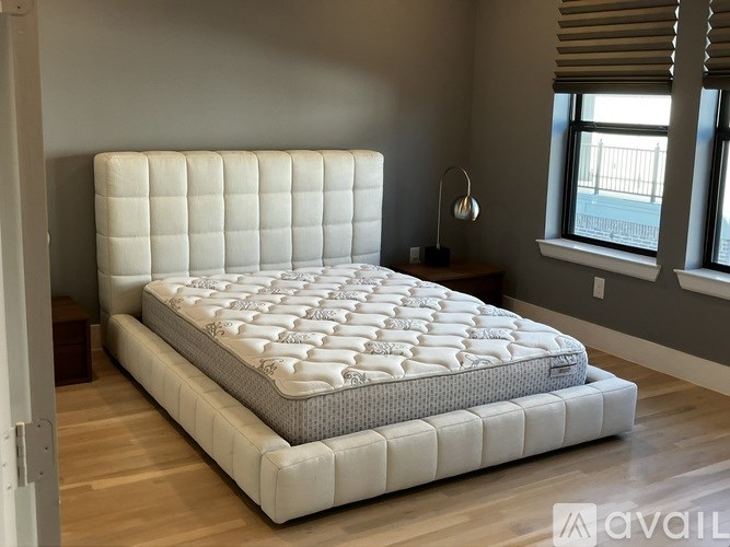 A large, white, tufted mattress is on display in a room with wooden flooring and a window.