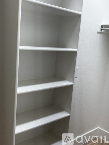A white shelving unit with five shelves is mounted on a white wall.