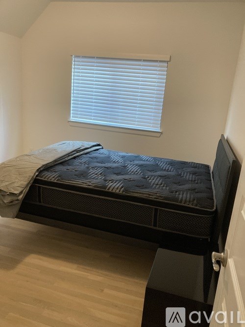 A bed with a black mattress and a grey blanket is in a room with a window.