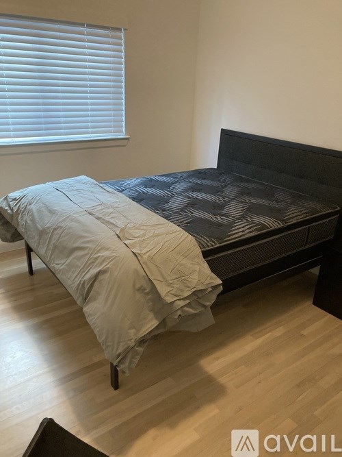 A bed with a black headboard and a grey blanket is in a room with wooden flooring.