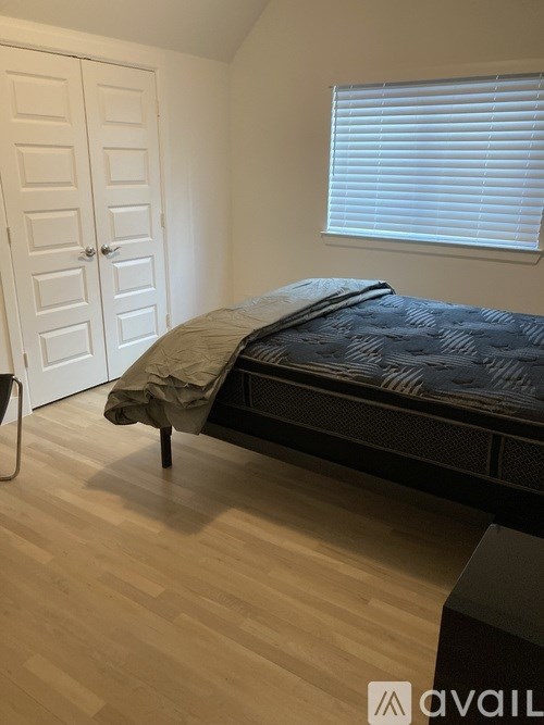 A bedroom with a bed, wooden floor, and a window with blinds.