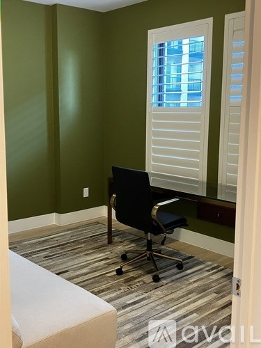A room with a black chair and a window with white shutters.