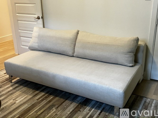 A white couch with two pillows sits in a room with a wooden floor and a white door.