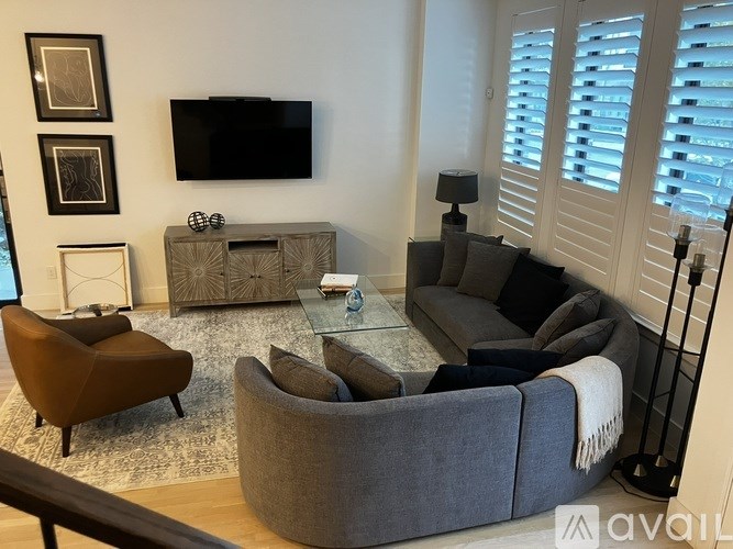 A living room with a grey sofa, a brown armchair, a wooden cabinet, a flat screen TV, and a rug.