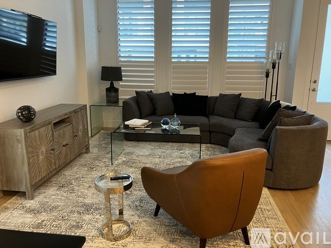 A living room with a grey couch, a brown chair, a glass coffee table, and a wooden cabinet.