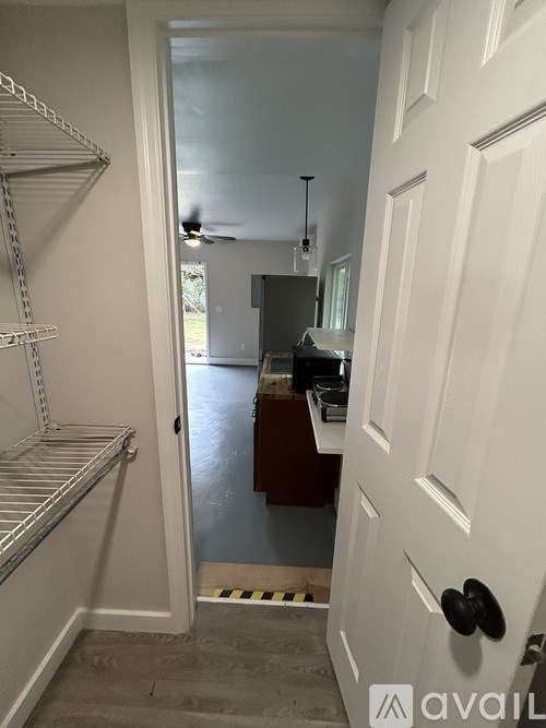A white door with a black handle is in the foreground of a room with a white wall and a metal shelving unit.