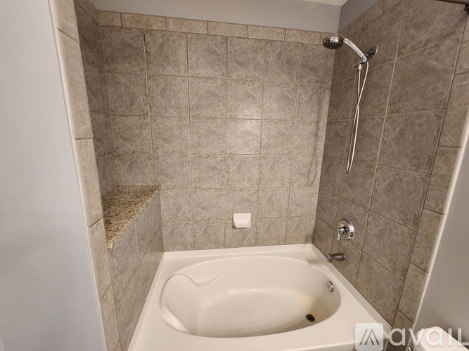 A beige bathtub is in a bathroom with tiled walls.