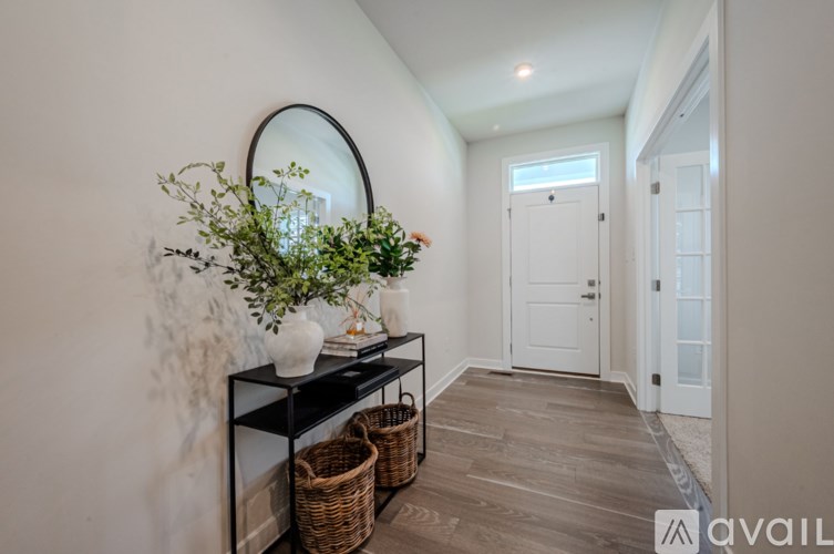 A hallway with a round mirror, a plant, and a basket on a black console table.