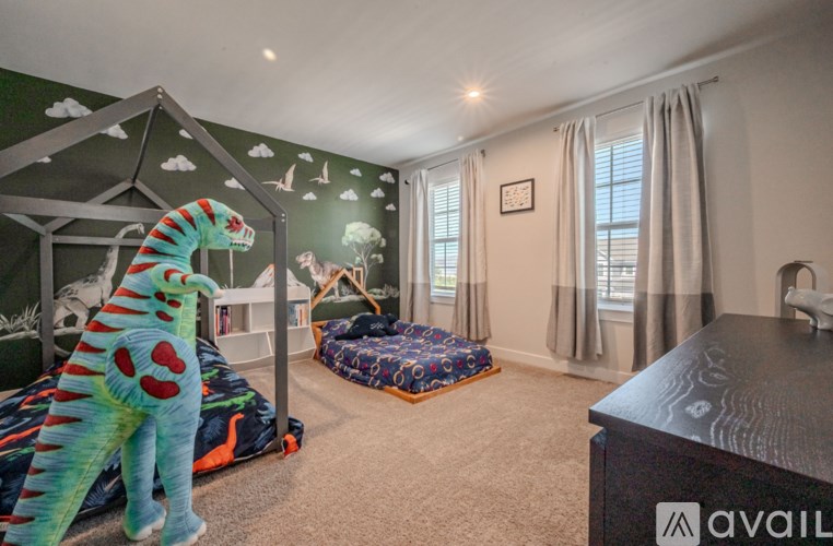 A room with a bed, a sofa, and a wall mural with a dinosaur.