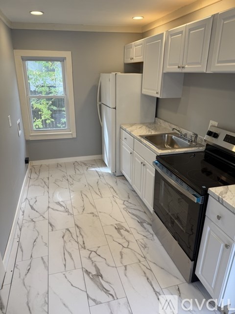 A kitchen with white cabinets and marble tiles on the floor.