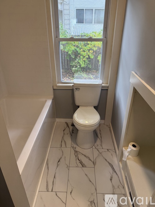 A white toilet in a bathroom with marble tiles and a window.