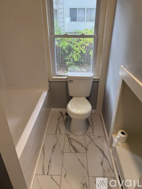 A white toilet in a bathroom with marble tiles and a window.