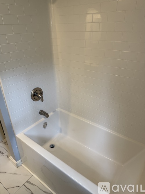 A white tiled bathroom with a white bathtub and a shower head.