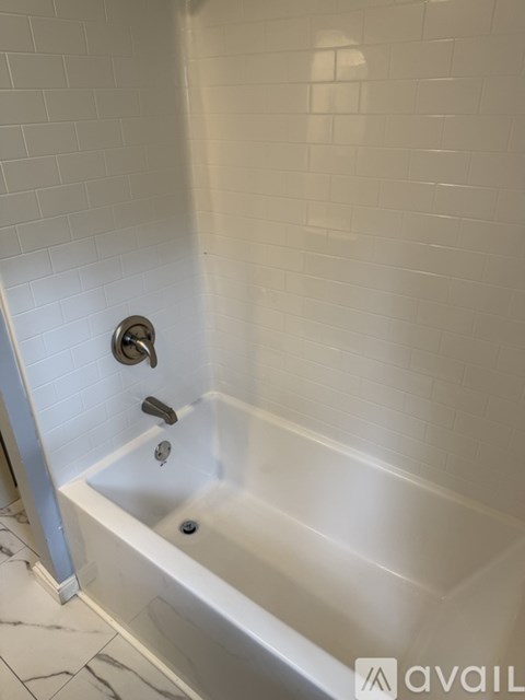 A white tiled bathroom with a white bathtub and a shower head.