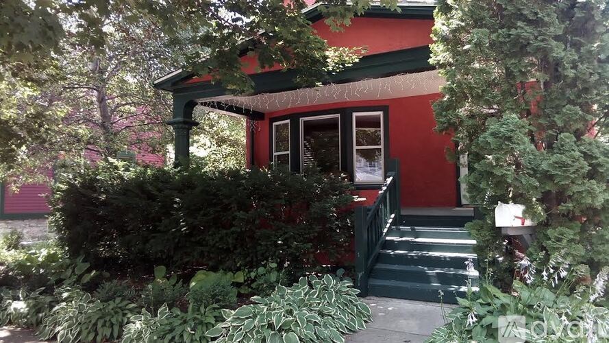 A red house with a green roof and a porch surrounded by trees.