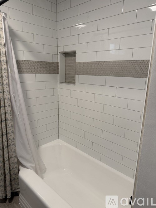 A white bathtub in a bathroom with grey tiles.