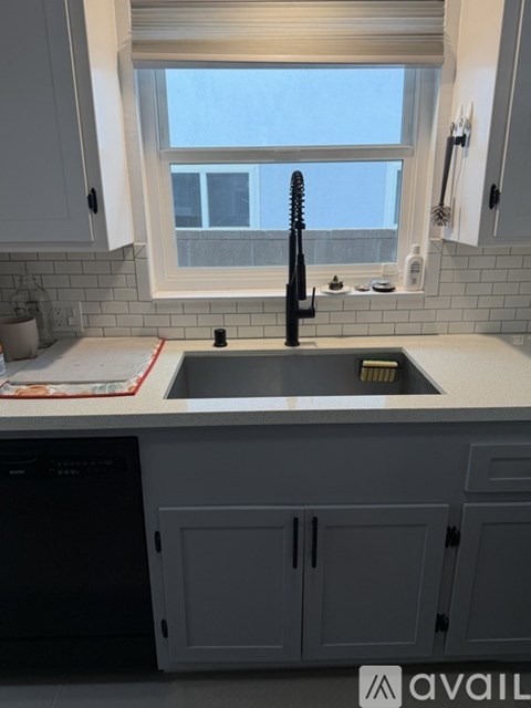 A kitchen with a black dishwasher and a window above the sink.