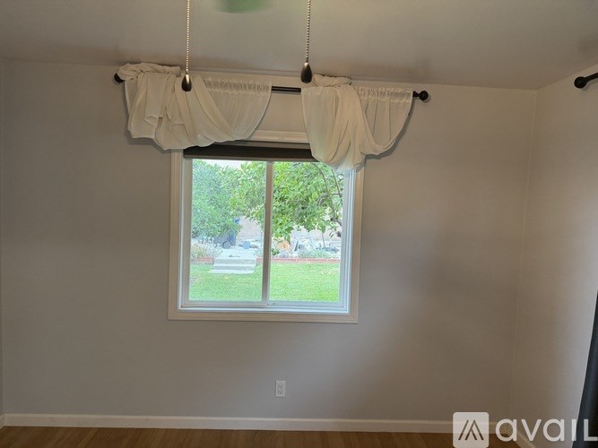 A window with white curtains and a view of a green lawn outside.