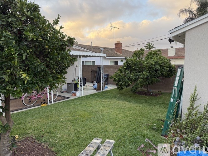 A backyard with a pink bicycle and a white fence.