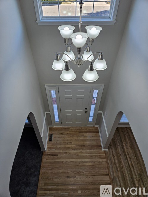A chandelier with white lamps hangs from the ceiling above a wooden staircase.